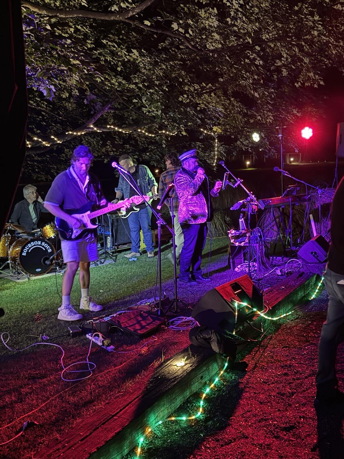 Live outdoor performance by a vibrant rock band under string lights, energizing a crowd at a nighttime event � perfect for weddings, parties, and special occasions in Queenstown and Central Otago.